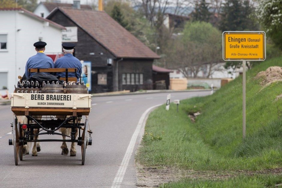 Ländliche Szene mit einem Pferdewagen und einem Brauerei-Schild.