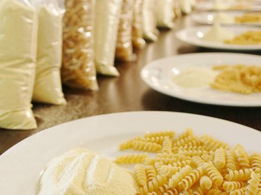 Plates with uncooked pasta and small bags of flour lined up on a table
