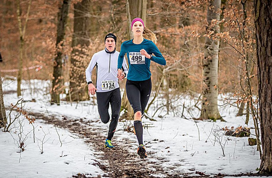 Zwei Läufer in Winterkleidung laufen auf einem verschneiten Waldweg