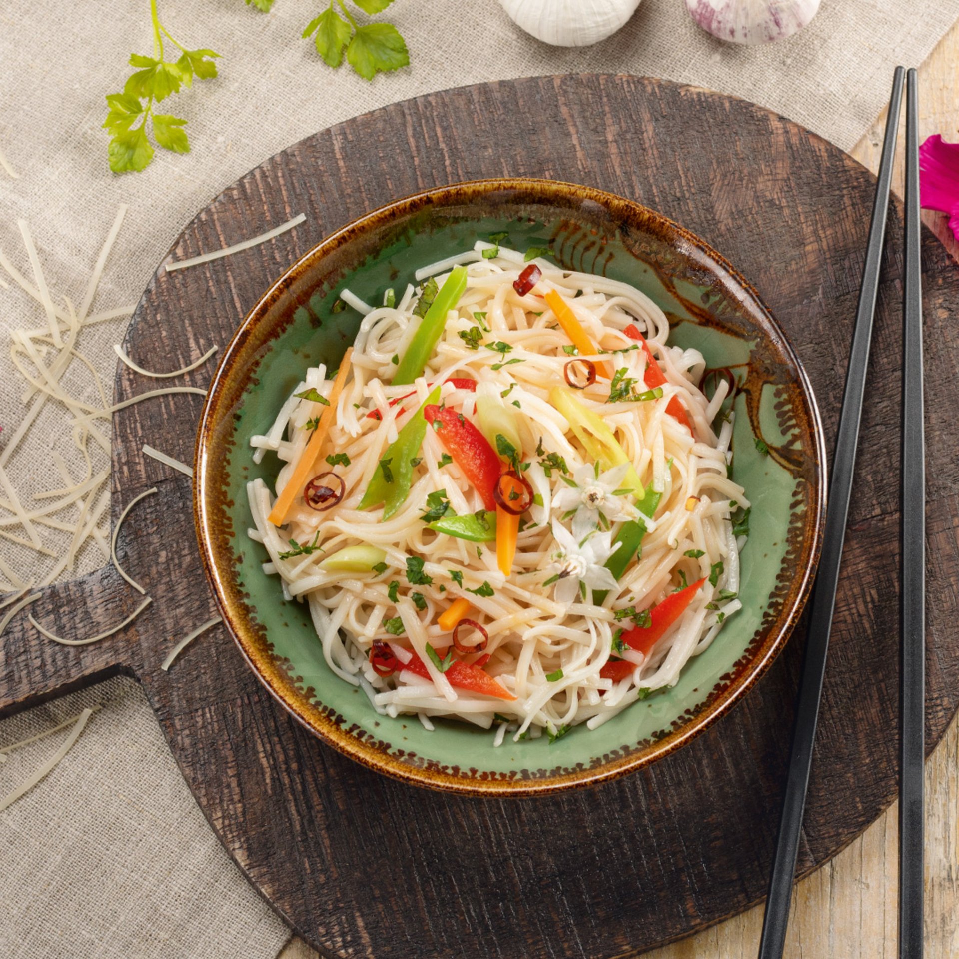 Bowl of rice noodles with sliced red chili, herbs, and lime wedges, served with chopsticks on a dark wooden surface