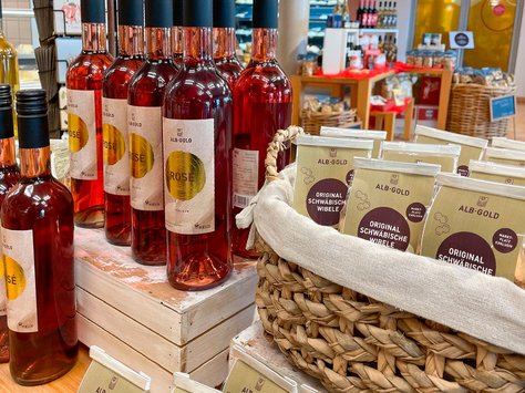 Mehrere Flaschen rosé Wein der Marke ALB-GOLD und ein Korb mit Original Schwäbischen Wibele Keksen in einer Verkaufsumgebung