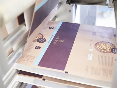 Printing machine producing a sheet with purple and beige design elements and circular logos