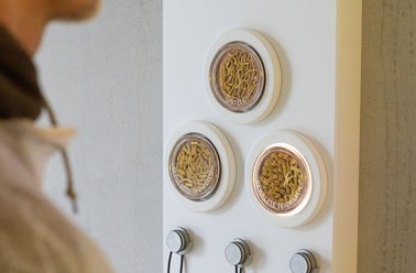 Drei durchsichtige an der Wand hängende Kreiselementen, die mit unterschiedlichen Rohstoffen gefüllt sind.