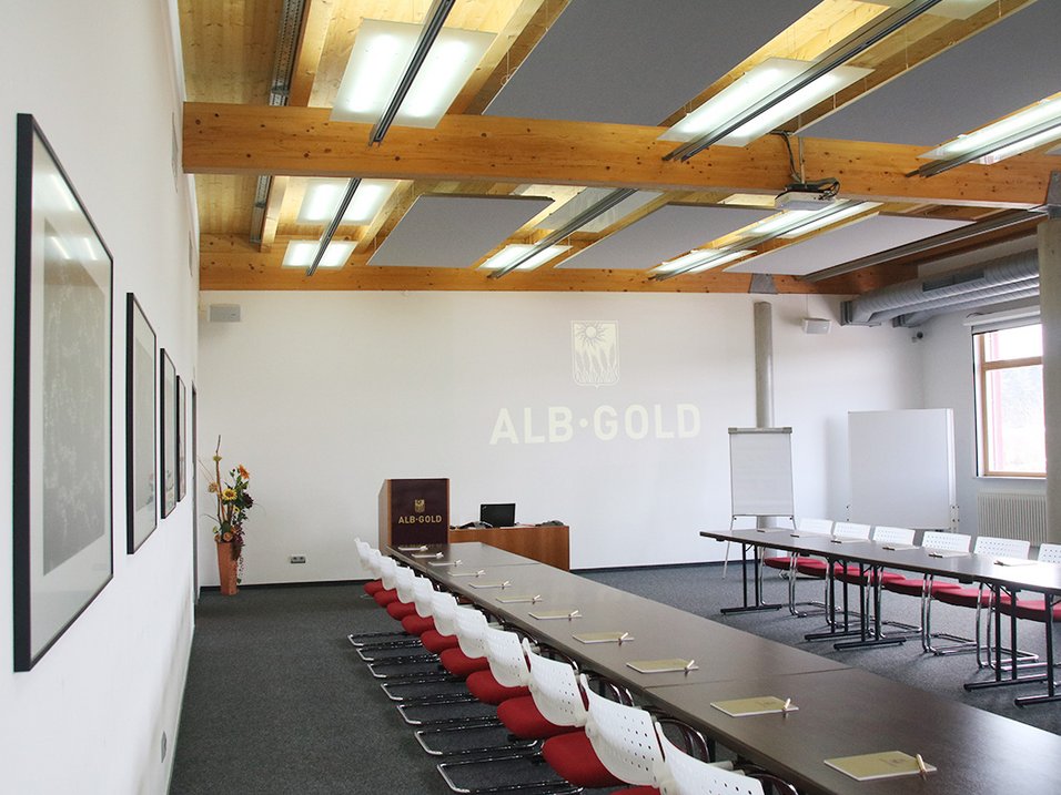 Konferenzraum mit langen Tischen, weißen Stühlen mit roten Sitzflächen, Flipcharts und ALB-GOLD-Logo an der Wand