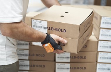 Person scannt mit Handscanner Karton mit Aufschrift 'ALB-GOLD' in Lager