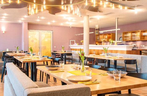 Modernes Restaurant mit Holztischen, grauen Sitzbänken, schwarzen Stühlen und frischen Blumen auf den Tischen