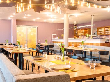 Bright modern restaurant interior with wooden tables set for dining and soft overhead lighting