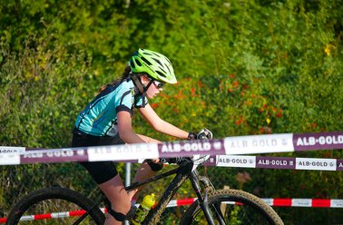 Jugendliche Radfahrerin mit grünem Helm und blauem Trikot bei Mountainbike-Rennen im Wald