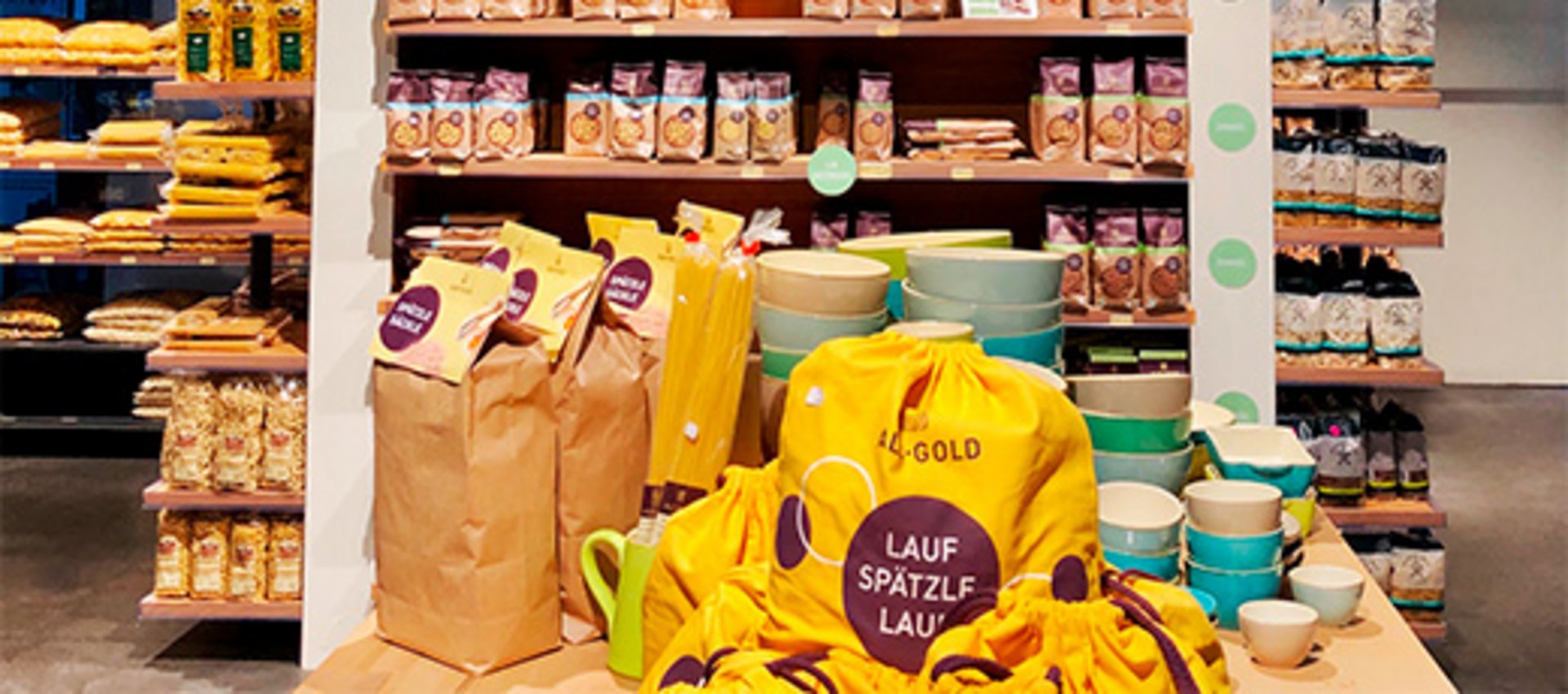 Regal mit verschiedenen Nudelsorten und gelben Stoffbeuteln mit Aufschrift 'Lauf Spätzle Lauf' in einem Lebensmittelgeschäft