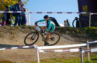 Mountainbiker in grüner Kleidung fährt auf einem abfallenden, mit Absperrband markierten Waldweg während eines Rennens