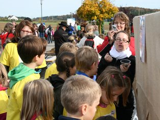 Kinder und Erwachsene versammeln sich draußen um eine Tafel mit Informationen