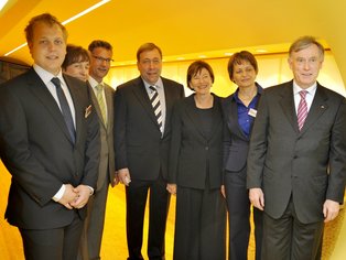 Sieben Personen in Businesskleidung befinden sich in einem gelb ausgeleuchteten Raum.