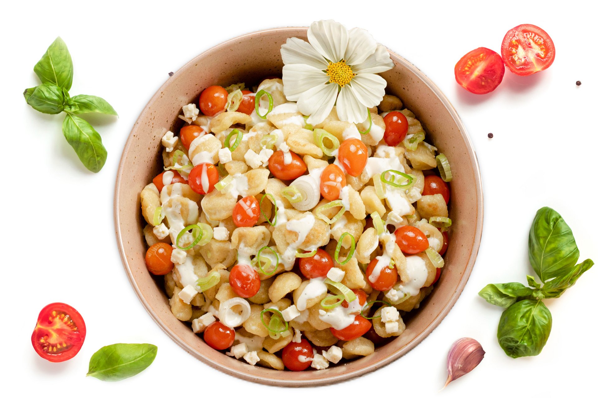 Schüssel mit bunter Pasta, Kirschtomaten, weißen Bohnen und frischem Basilikum, garniert mit einer weißen Blume