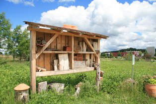 Wildbienenhaus aus Holz mit verschiedenen Nistmaterialien in einer grünen Wiese unter blauem Himmel