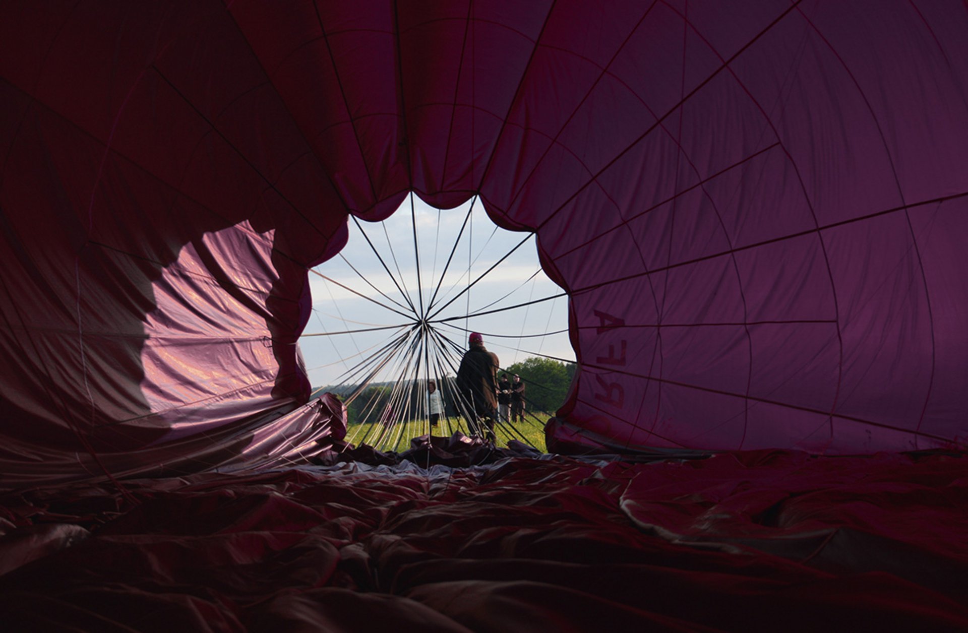 Blick aus dem Inneren eines aufgeblasenen Heißluftballons auf zwei Personen und eine grüne Landschaft im Hintergrund