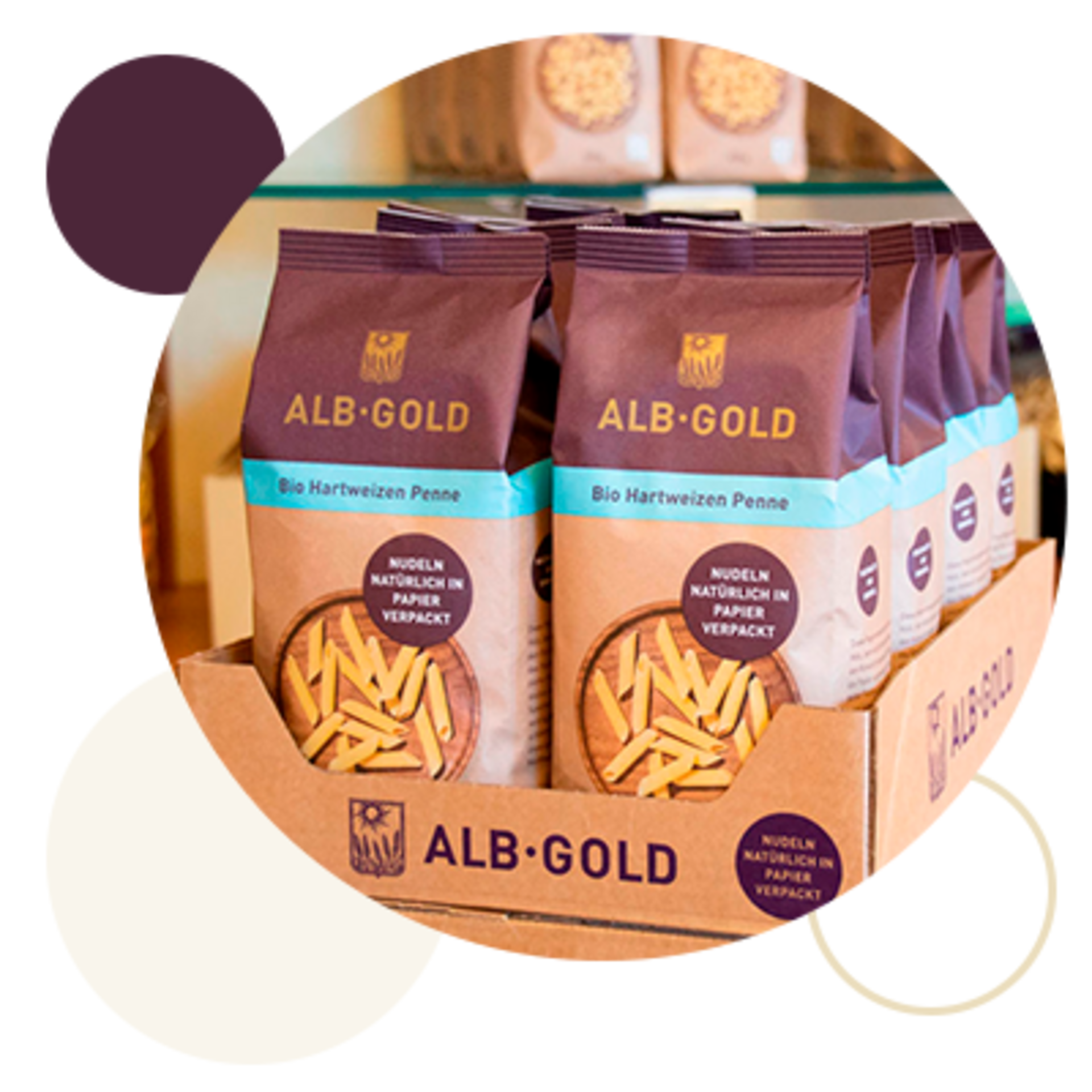 Mehrere Packungen ALB-GOLD Bio Hartweizen Penne, natürlich in Papier verpackt, in einem Karton aufgereiht