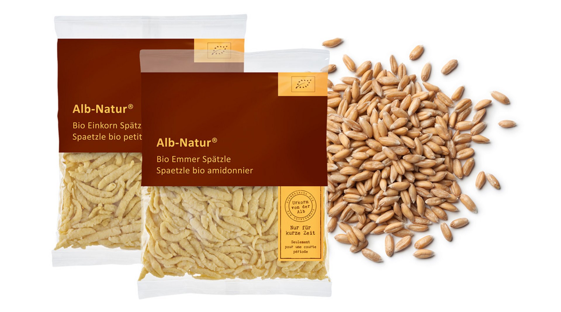 Zwei Verpackungen der Marke Alb-Natur, im Hintergrund befinden sich Körner des Rohstoffs.