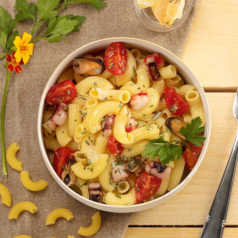 Bunter Nudelsalat mit Tomaten, Basilikum und Käse in einer Schüssel auf einem Tisch