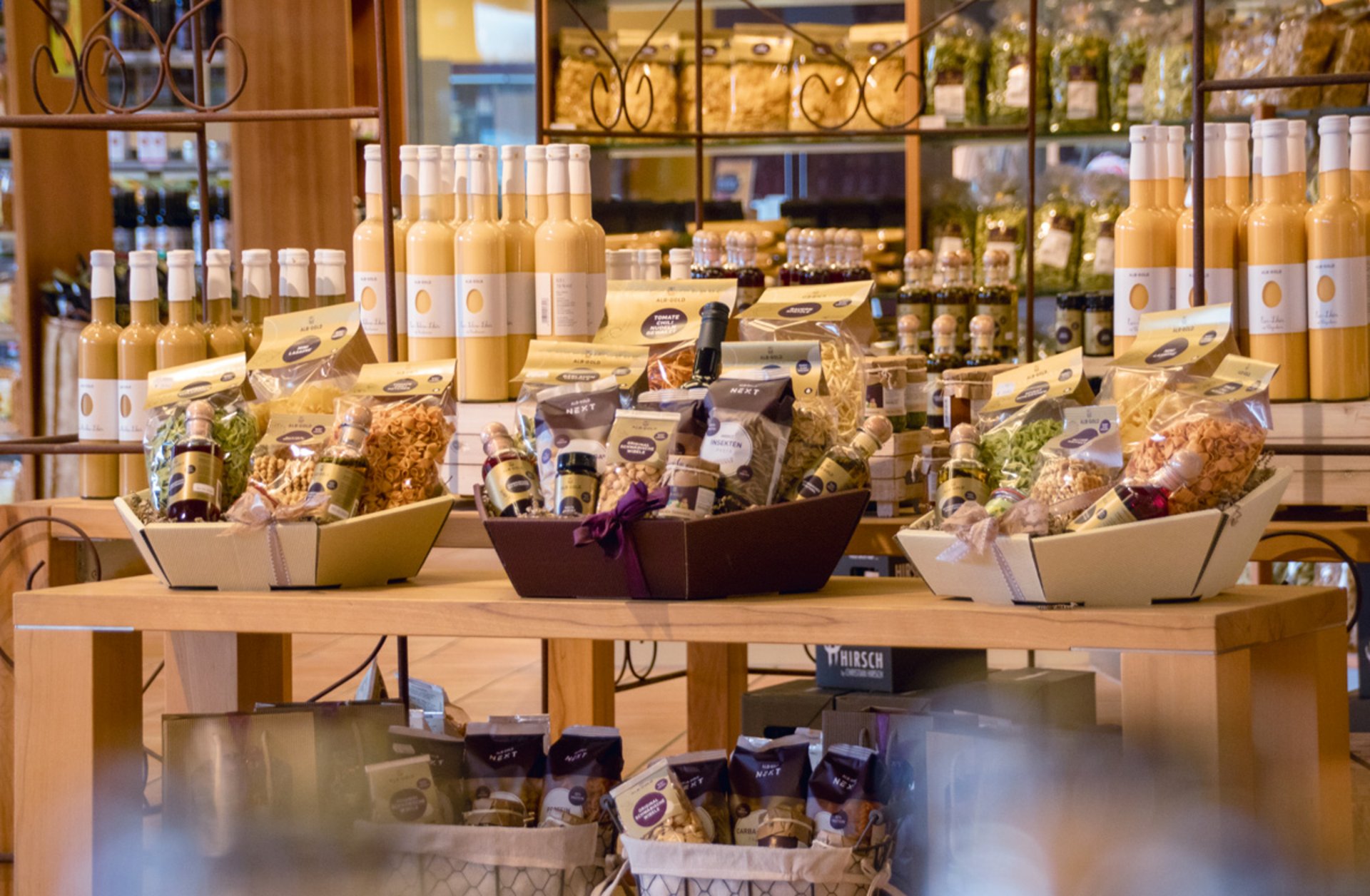 Tisch mit verschiedenen Produkten, darunter Flaschen mit gelbem Eierlikör und Körbe mit verpackten Lebensmitteln in einem Laden