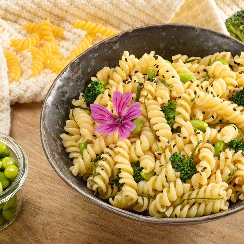 Schüssel mit Fusilli-Nudelsalat, garniert mit grünen Erbsen und einer essbaren Blume