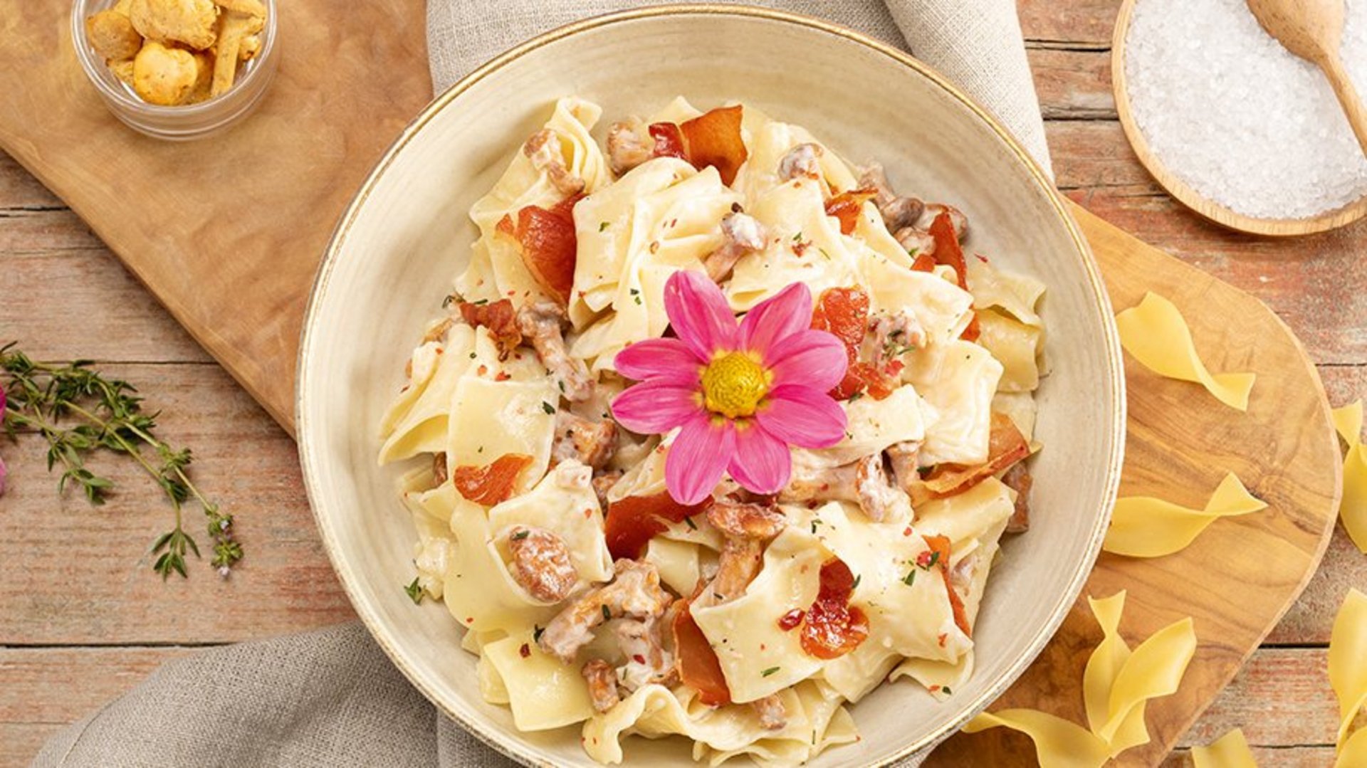 Bandnudeln mit cremiger Sahnesauce und Pilzen, garniert mit einer essbaren Blume auf einem weißen Teller