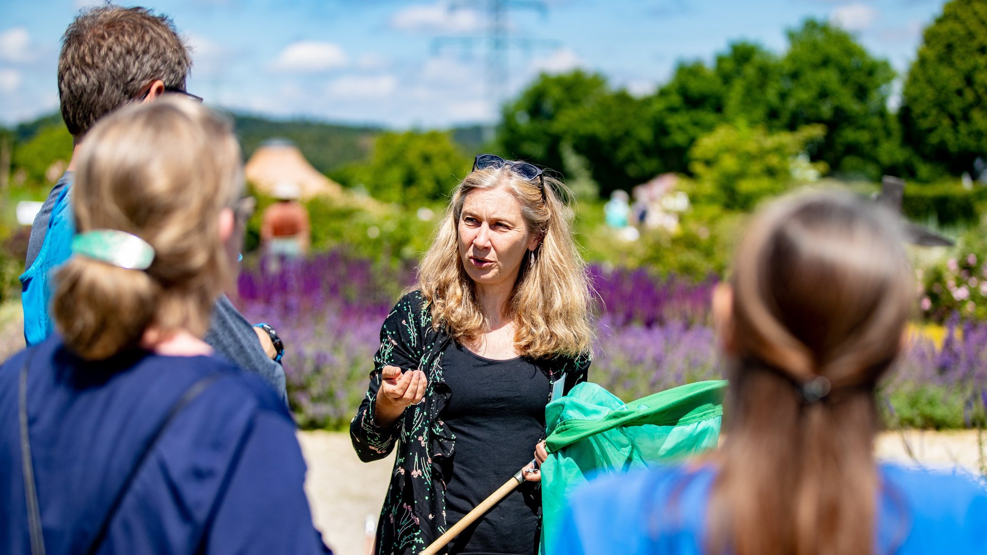 Eine Frau erklärt während einer Gartenführung mit einem Netz in der Hand.
