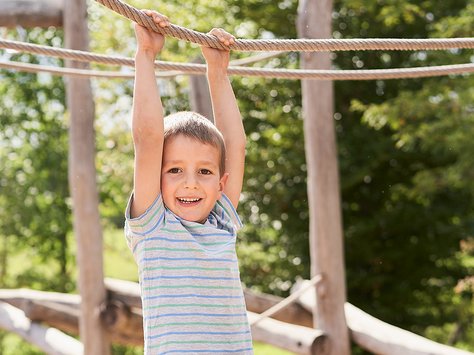 Junge in gestreiftem T-Shirt hängt an einem Kletterseil im Freien und lächelt