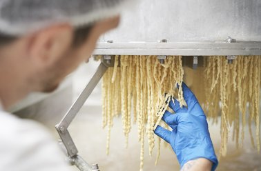 Lebensmitteltechniker mit blauen Handschuhen überprüft frische Pasta, die aus einer Maschine kommt