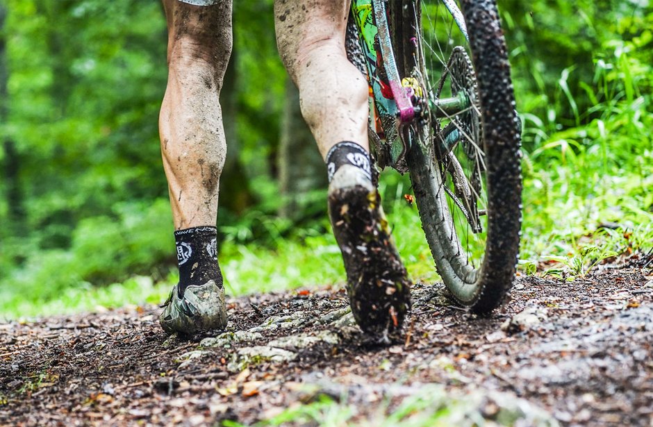 Ein Mountainbike-Fahrer mit schmutzigen Beinen auf einem Waldweg.