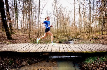 Mann in Sportkleidung läuft über eine Holzbrücke im Wald im Frühling