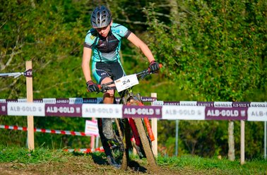 Mountainbiker in grünem Trikot fährt auf Waldweg bei Rennen mit Absperrband