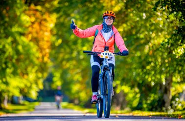 Frau in Sportkleidung und Helm fährt Fahrrad auf einem von Bäumen gesäumten Weg im Herbst