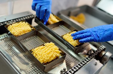 Maschine formt die rechteckigen Nudelkuchen der Mie-Noodles, Bediener trägt blaue Handschuhe