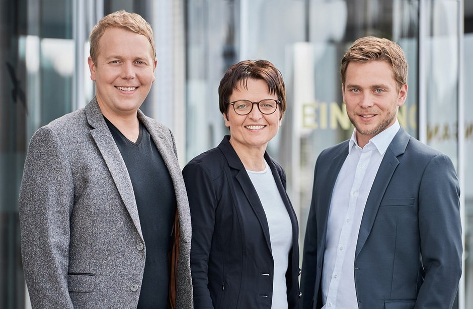Three CEOs standing together in business attire, smiling in a modern office setting