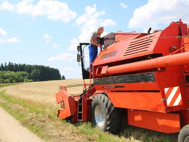Red combine harvester working on a field under a partly cloudy sky