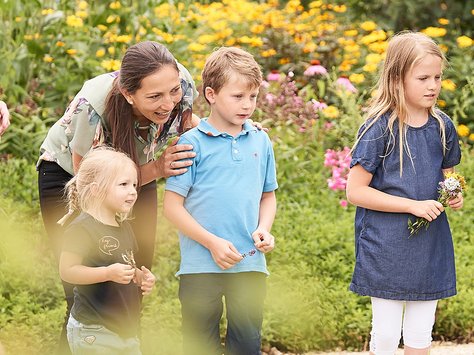 Frau mit drei Kindern in einem Garten, zwei Kinder halten Blumen, alle schauen nach rechts
