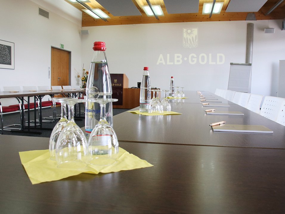 Konferenzraum mit langem Tisch, Wasserflaschen, Gläsern und Schreibutensilien, Wand mit Schriftzug 'ALB-GOLD'