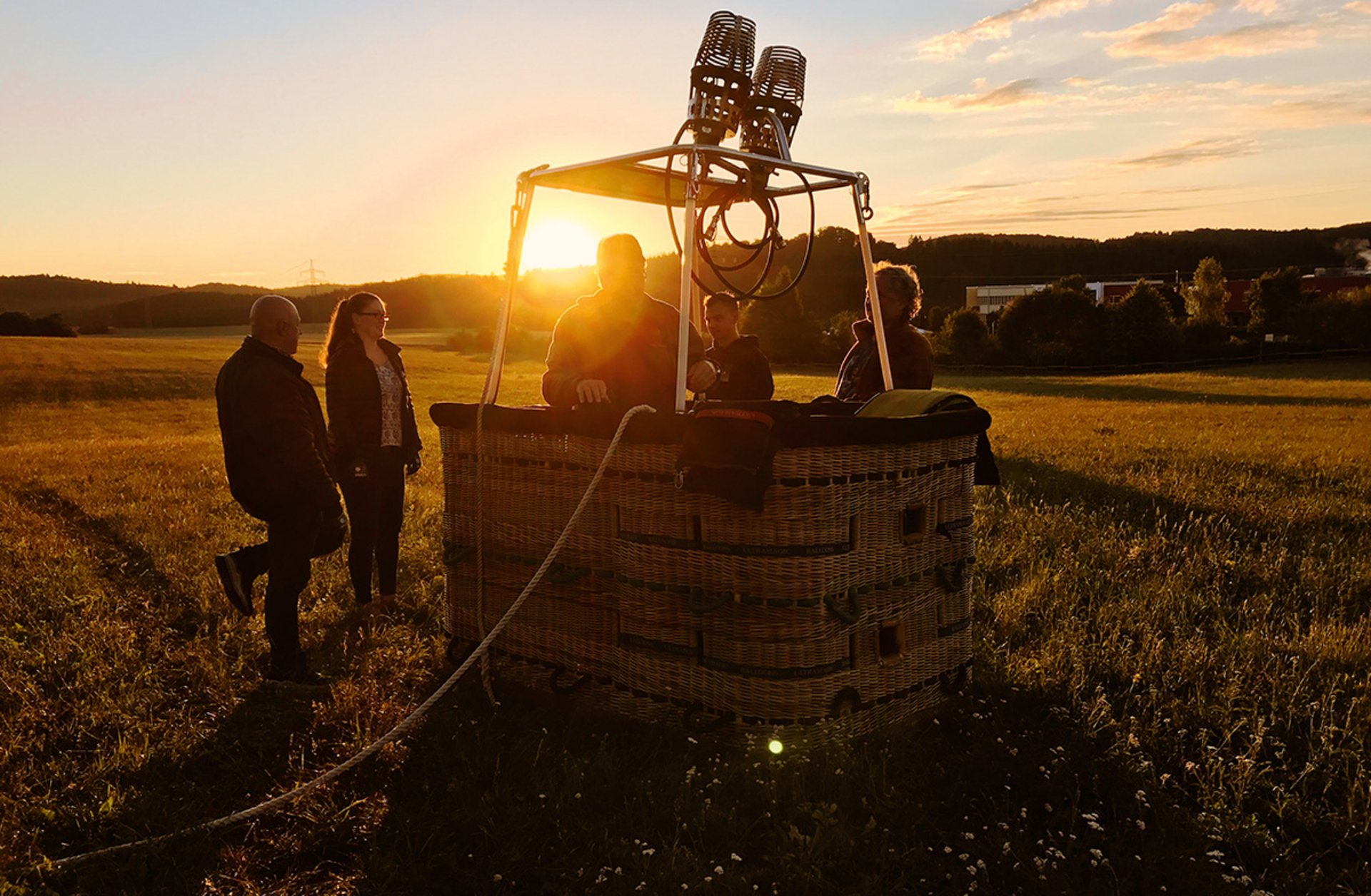 Heißluftballonkorb mit zwei Personen bei Sonnenuntergang auf einem Feld