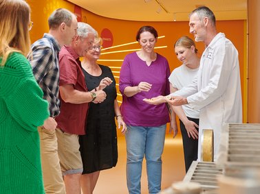 Group of six adults standing indoors, smiling and interacting in a casual setting