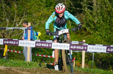 Mountainbiker in grünem Trikot und Helm fährt auf Waldweg bei Rennen mit Absperrband