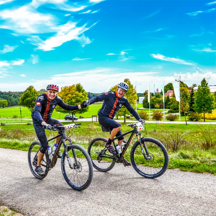 Zwei Radfahrer fahren auf einem Weg durch eine grüne Landschaft bei sonnigem Wetter