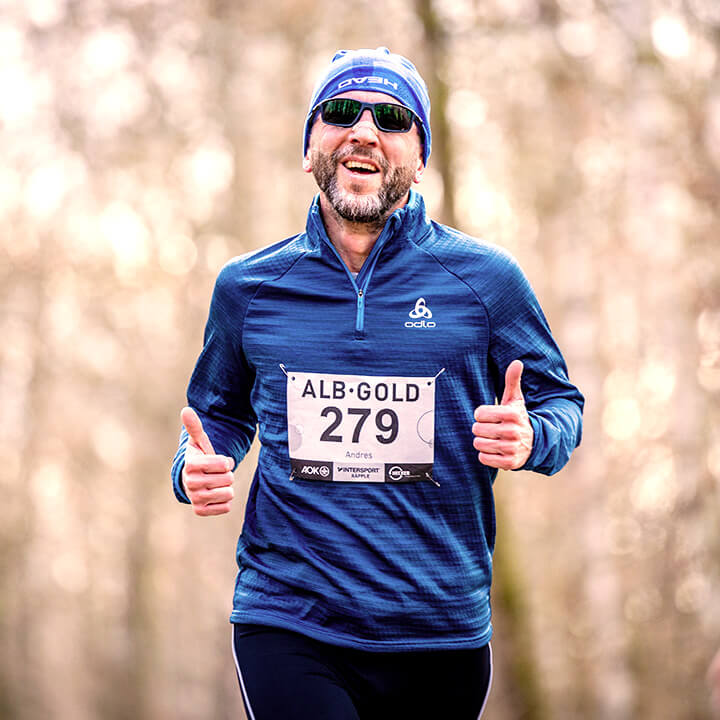 Mann in blauer Sportkleidung und Sonnenbrille läuft im Wald, trägt Startnummer 279