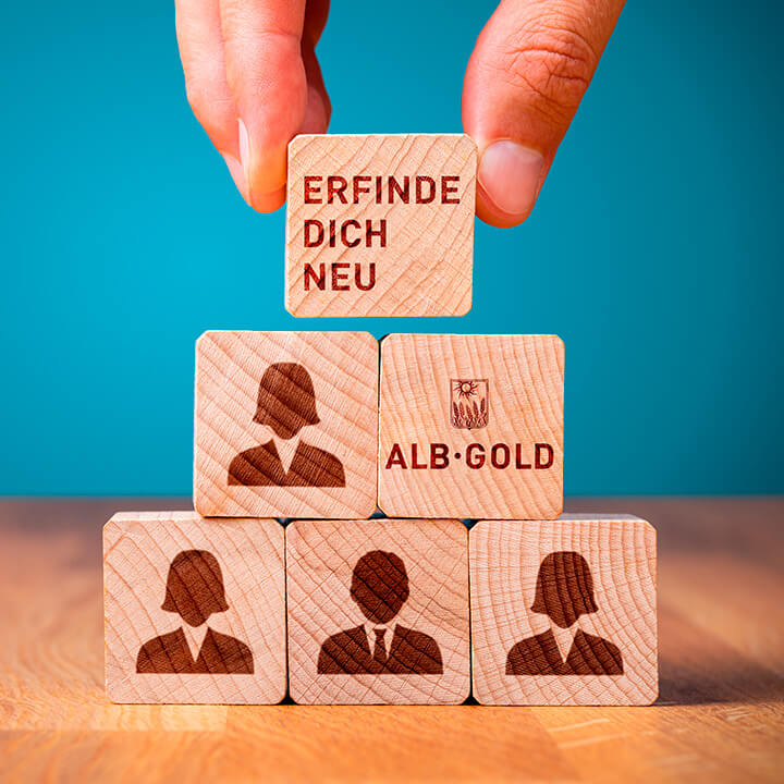 Holzklötze mit der Aufschrift 'Erfinde dich neu' und Figuren, die Kreativität symbolisieren.